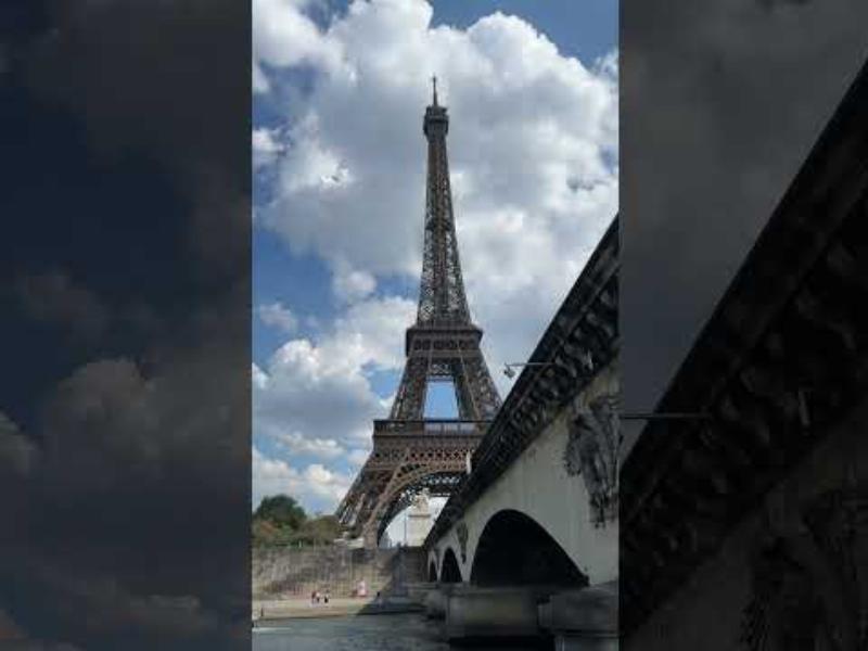 Des touristes profitant d'une vue panoramique de Paris depuis un bus, avec la Seine et des monuments en arrière-plan